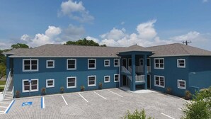 Un bâtiment à deux étages, à la façade bleue, doté d’un parking comprenant des places réservées aux personnes handicapées, et d’un escalier menant à l’entrée.