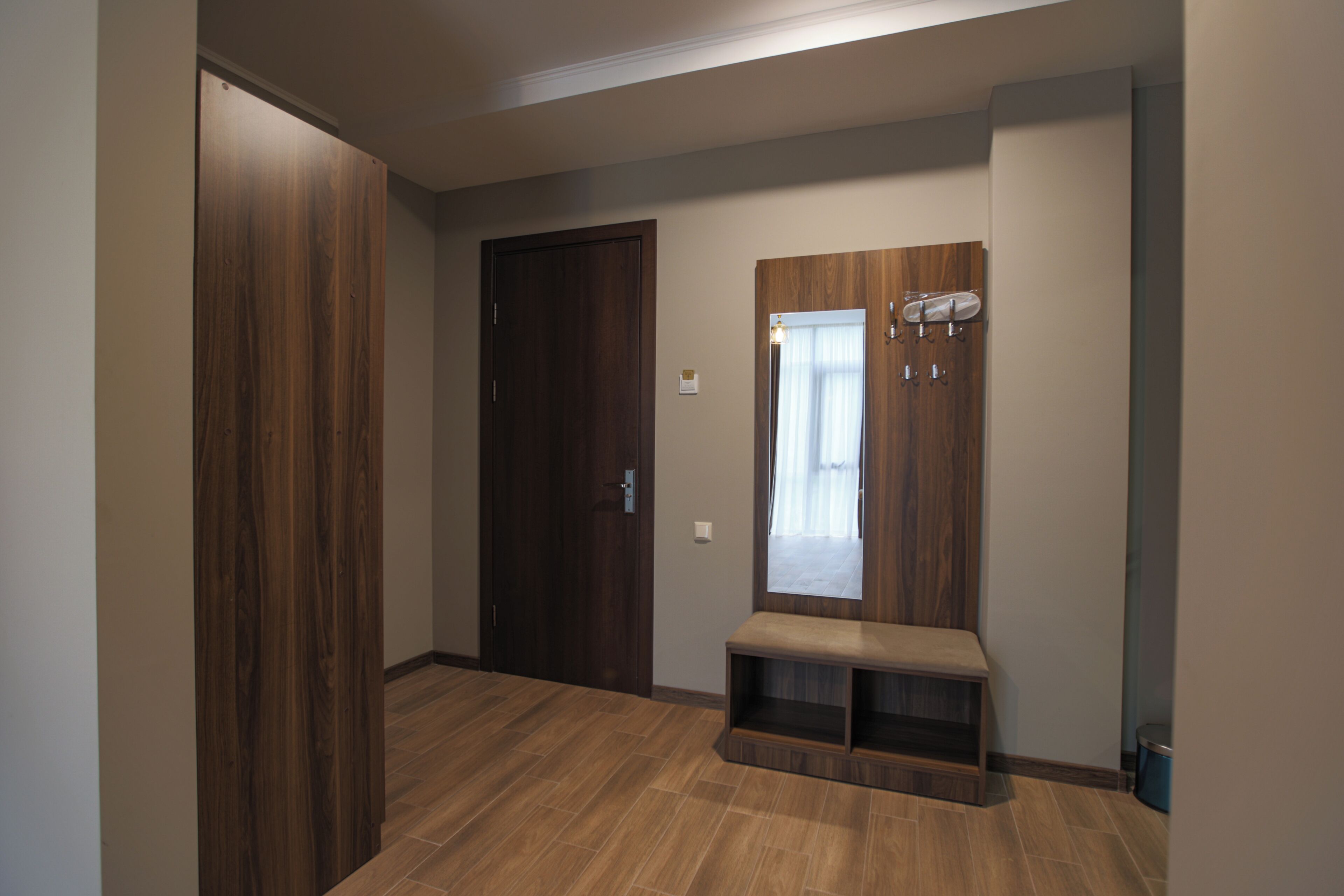 Un pasillo con suelo de madera, una puerta cerrada y un banco con espejo.