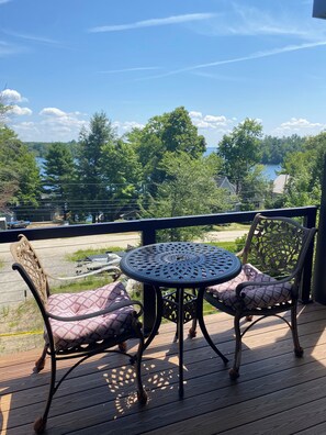 Una terraza con dos sillas y una mesa, con vista a un lago y árboles.