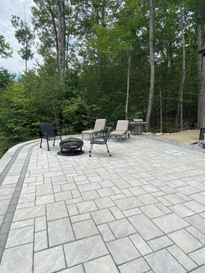 Un espace patio avec un foyer, des sièges d’extérieur et une vue sur une zone boisée.