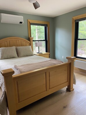 Un dormitorio con una cama de madera, una mesita de noche, una lámpara y una ventana con vistas a árboles.
