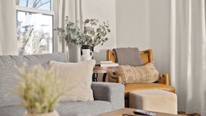 Un salon avec un canapé gris, une table basse en bois et une petite table d’appoint sur laquelle est posé un vase rempli de plantes vertes.