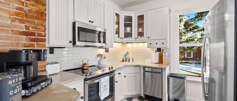 A kitchen with white cabinets, a stainless steel refrigerator, a microwave, and a coffee maker.