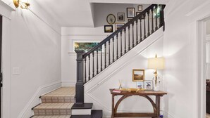 Un escalier doté d’une balustrade noire et de marches recouvertes d’une moquette beige, menant à un palier où se trouvent une console en bois et une lampe.
