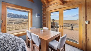 A wooden dining table with chairs in a room with large windows overlooking a mountainous landscape. - Henry's Hideaway Cabin (Red Lodge)