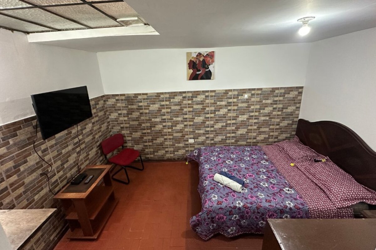 A bedroom with a bed, a desk, a chair, and a television mounted on the wall.