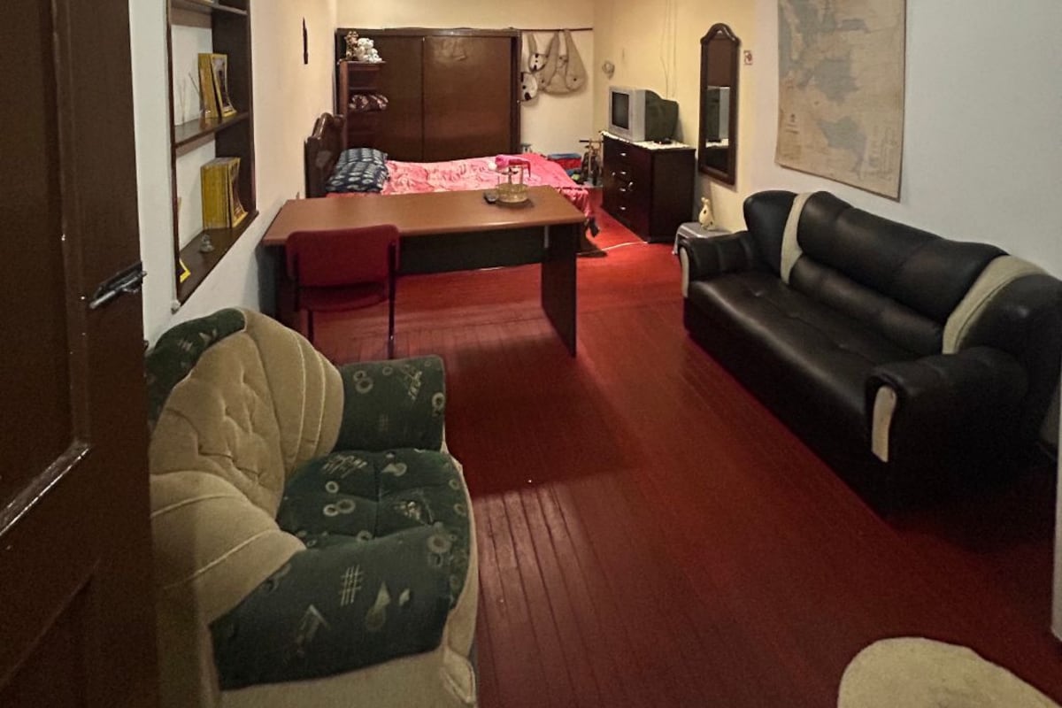 A room with a red carpet, a sofa, a table, a television, and a wardrobe.