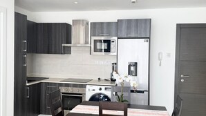 A modern kitchen with dark cabinets, a microwave, a refrigerator, a stove, and a dining table with chairs. - 2 bedroom duplex apartment (Accra)