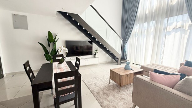 A modern living room with a dining area, a staircase, and a large window with curtains. - 2 bedroom duplex apartment (Accra)
