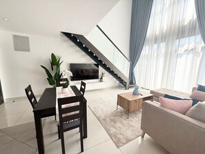 Ein modernes Wohnzimmer mit Essbereich, einer Treppe und einem großen Fenster mit Vorhängen.