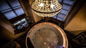 Un jacuzzi con una araña colgante, una ventana con persianas y una mesita con un adorno decorativo.