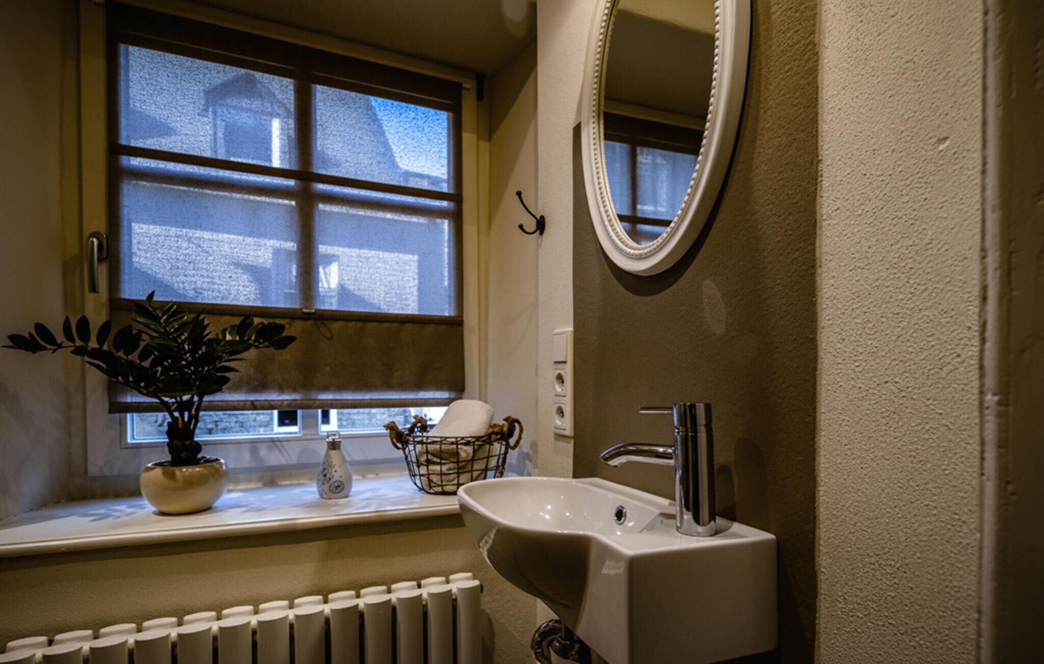 Ein Badezimmer mit Fenster, Waschbecken, Spiegel und Heizkörper.