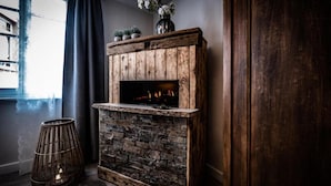 Una chimenea rústica con fachada de piedra y marco de madera, una cesta tejida y un jarrón con flores encima.