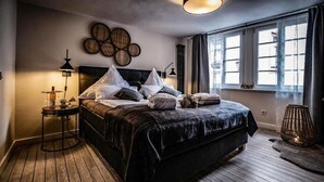 Un dormitorio con una cama grande, una mesita de noche, una lámpara y un ventanal con cortinas.