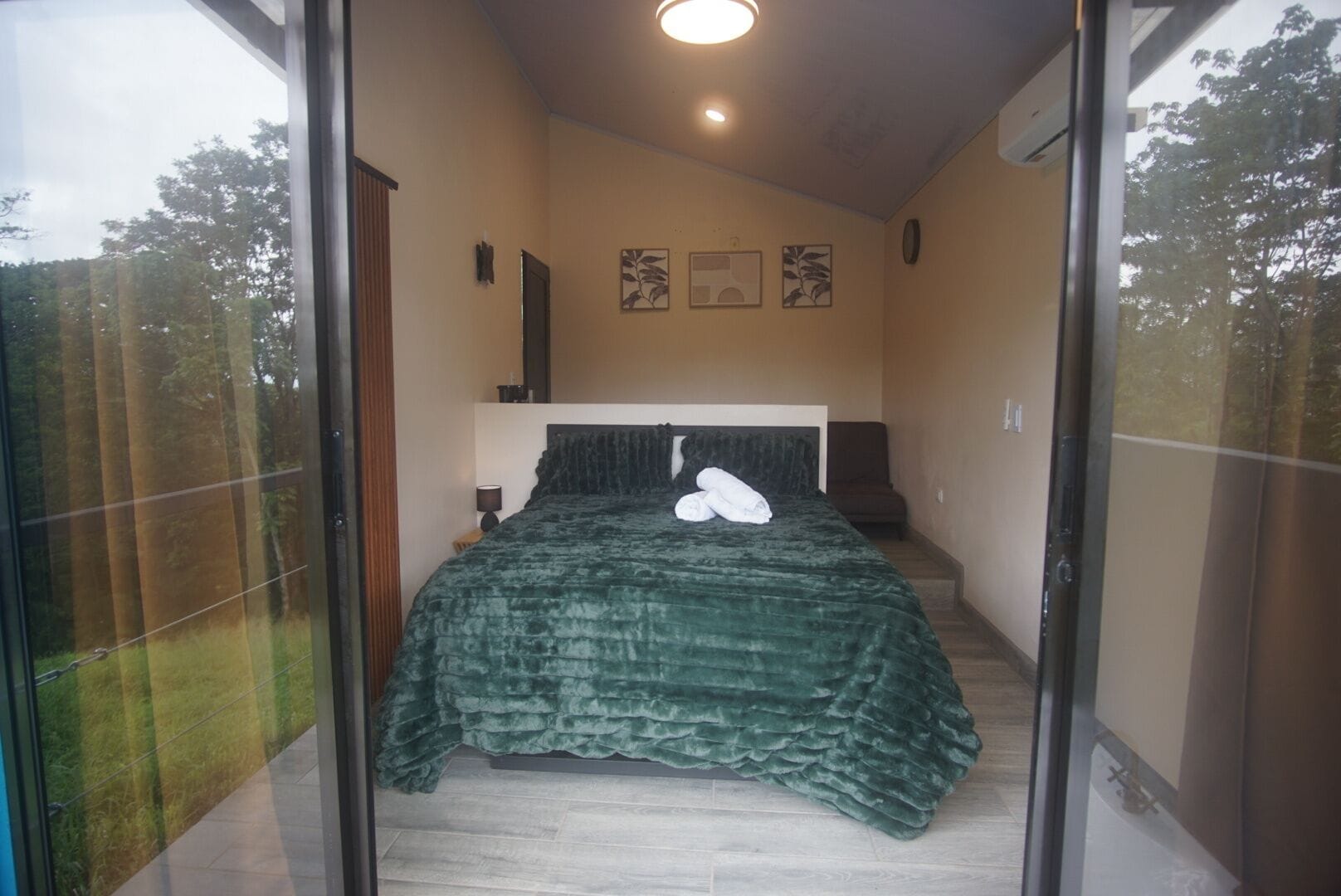 A bedroom with a bed, a nightstand, a lamp, and a window with a view of trees.