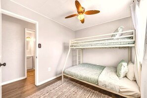 Een kamer met een stapelbed, een plafondventilator, een deur naar een andere kamer en een kamerbreed tapijt met een patroon.