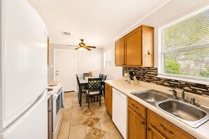A compact kitchen with a dining area, a ceiling fan, and a window with blinds. - Mins to Fort Sill•Wichita Mountains•Kid Friendly•Prime Central Location! (Lawton)