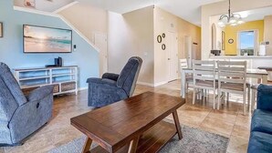 A living room with a sofa, a coffee table, and a TV. There is a staircase leading to another level. - Regal Palms 4BR Getaway • Resort Stay • Great for Families (Davenport)