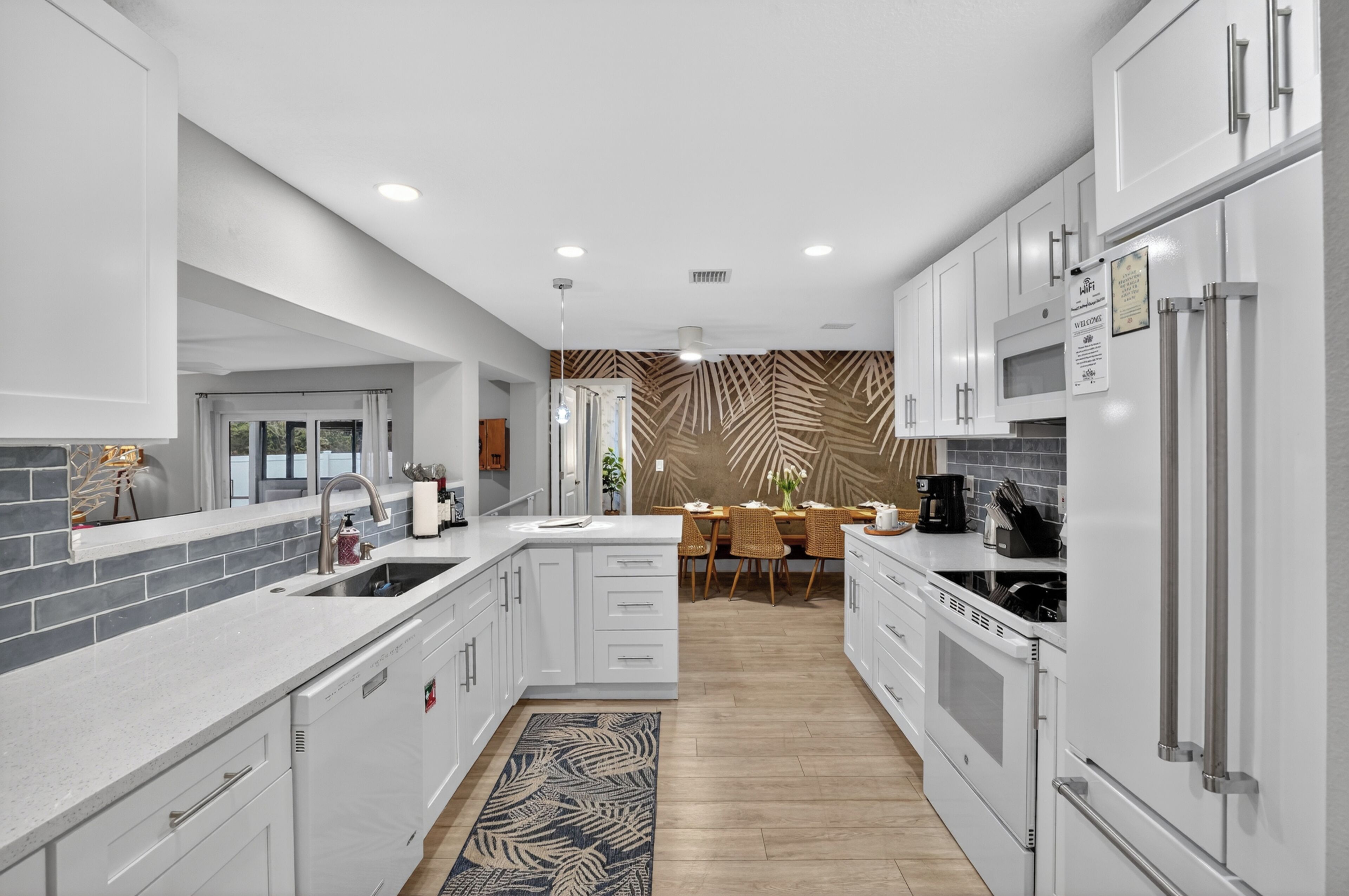 A modern kitchen with white cabinetry, a central island, and a dining area with a patterned wall.