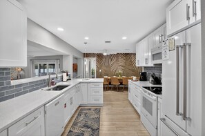 A modern kitchen with white cabinetry, a central island, and a dining area with a patterned wall. - Relaxing Pool-Fire Pit-Putt-Putt-Pool Table-Air Hockey-PingPong-5 miles to AMI (Bradenton)