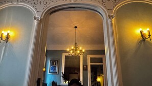 Un pasillo arqueado con candelabros, un comedor con sillas y una mesa, y un umbral que da a otra habitación.