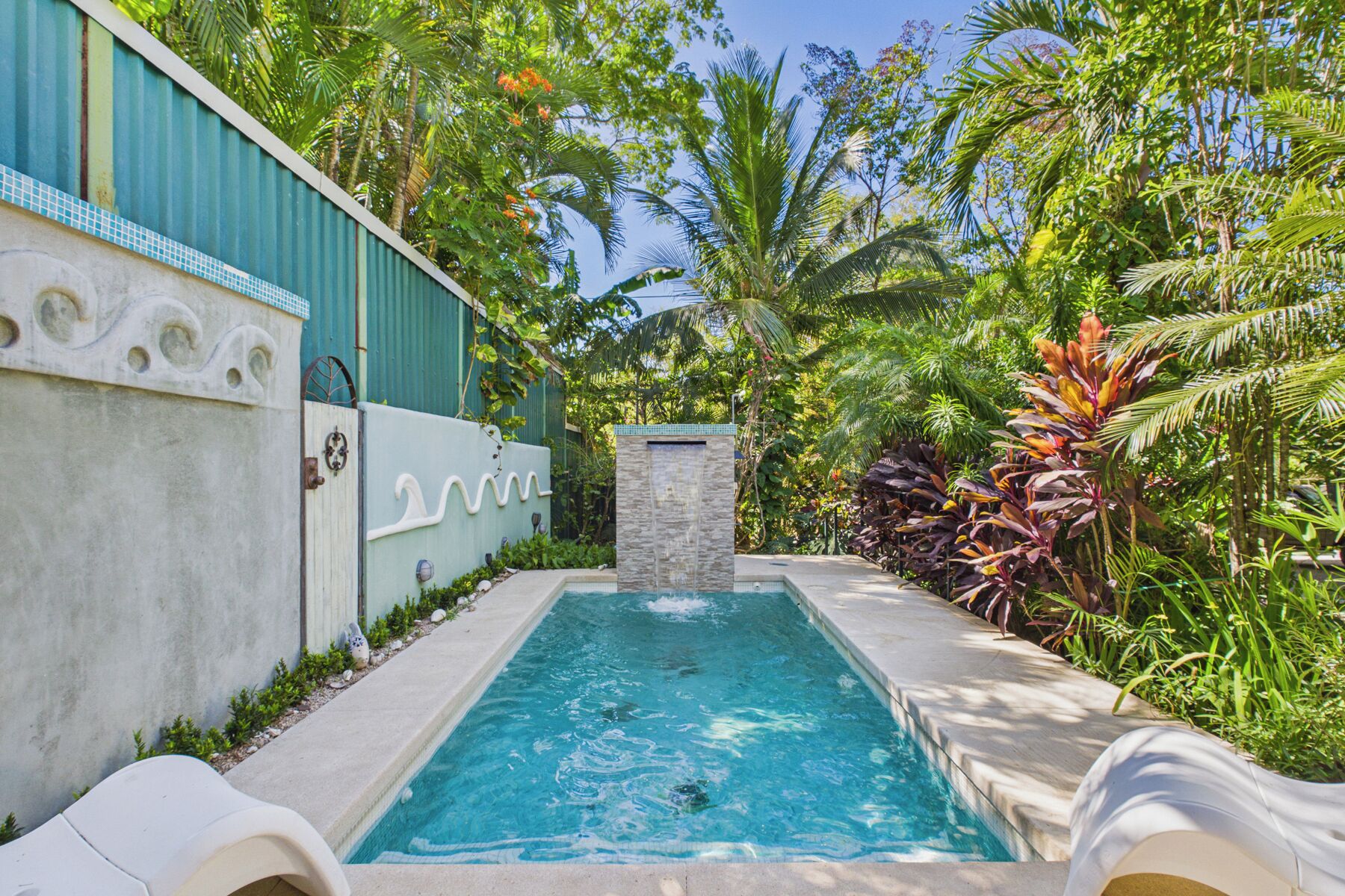 Une piscine agrémentée d’une cascade, entourée d’une végétation tropicale luxuriante et d’un mur décoratif.