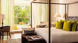 A hotel room with a four-poster bed, a sitting area with a chair and a small table, a large window with curtains, and a view of greenery outside. - Beachfront Grand Luxxe Spa Suite 3 BEDRM (Nuevo Nayarit)