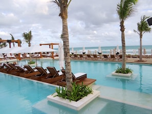A poolside area with lounge chairs and umbrellas, palm trees, and a view of the ocean. - Beachfront Grand Luxxe Spa Suite 3 BEDRM (Nuevo Nayarit)