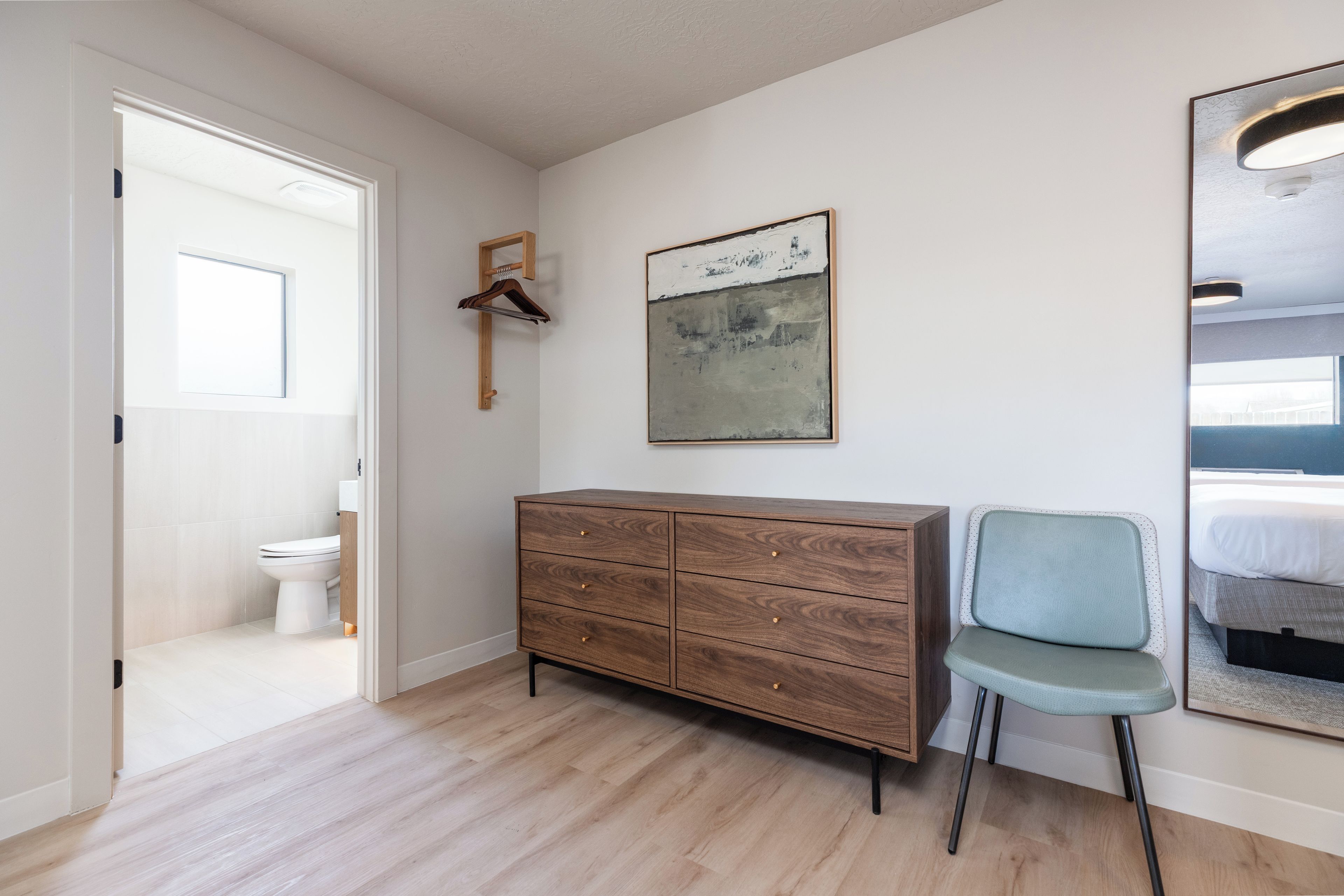 Une pièce comprenant une commode en bois, une chaise, un tableau et un lit avec une tête de lit.