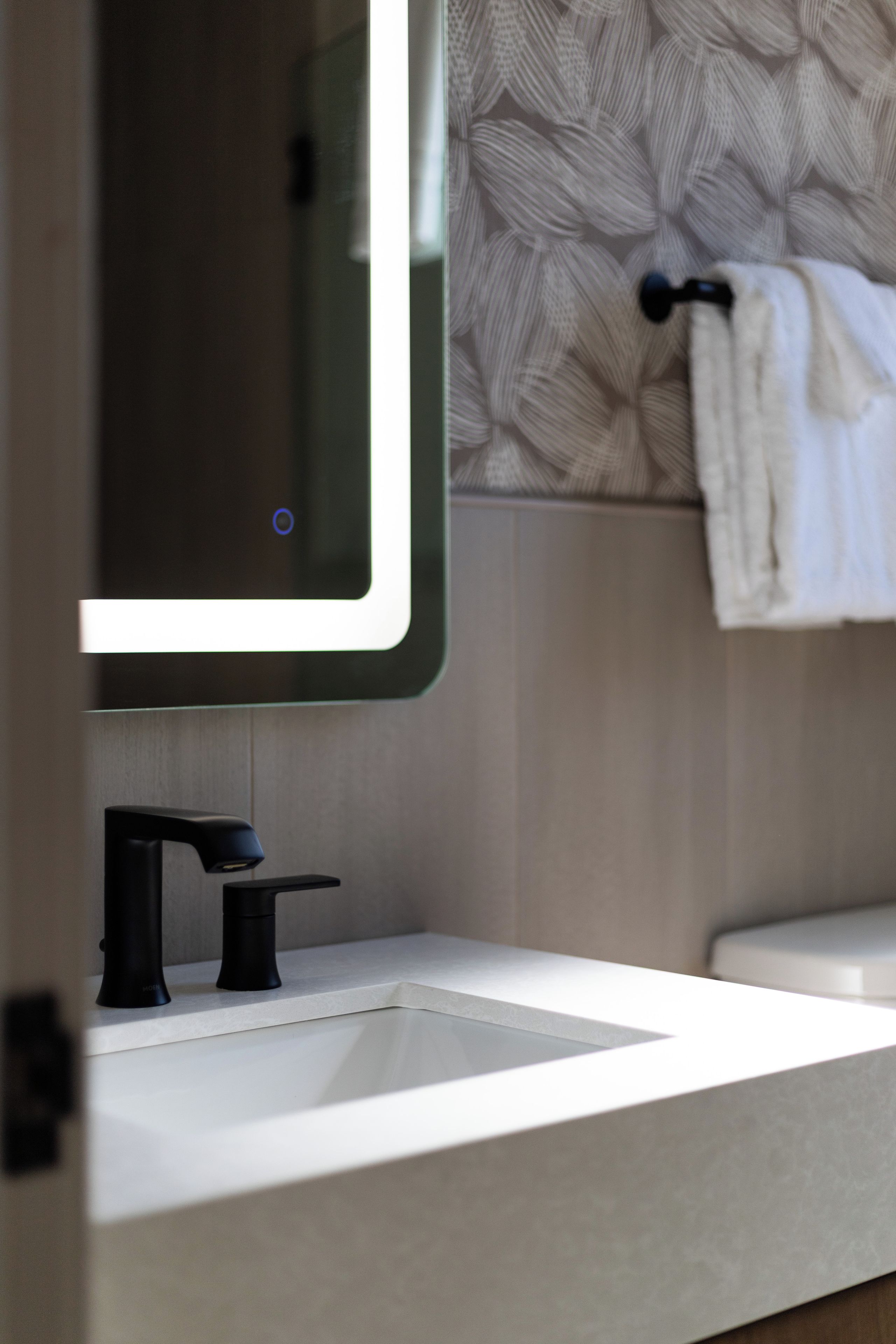 Un baño con un lavamanos moderno, un espejo y un perchero para toallas.