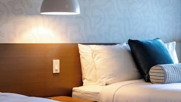 Hotellihuone, jossa on sänky, yöpöytä, lamppu ja kuviollinen tapetti.