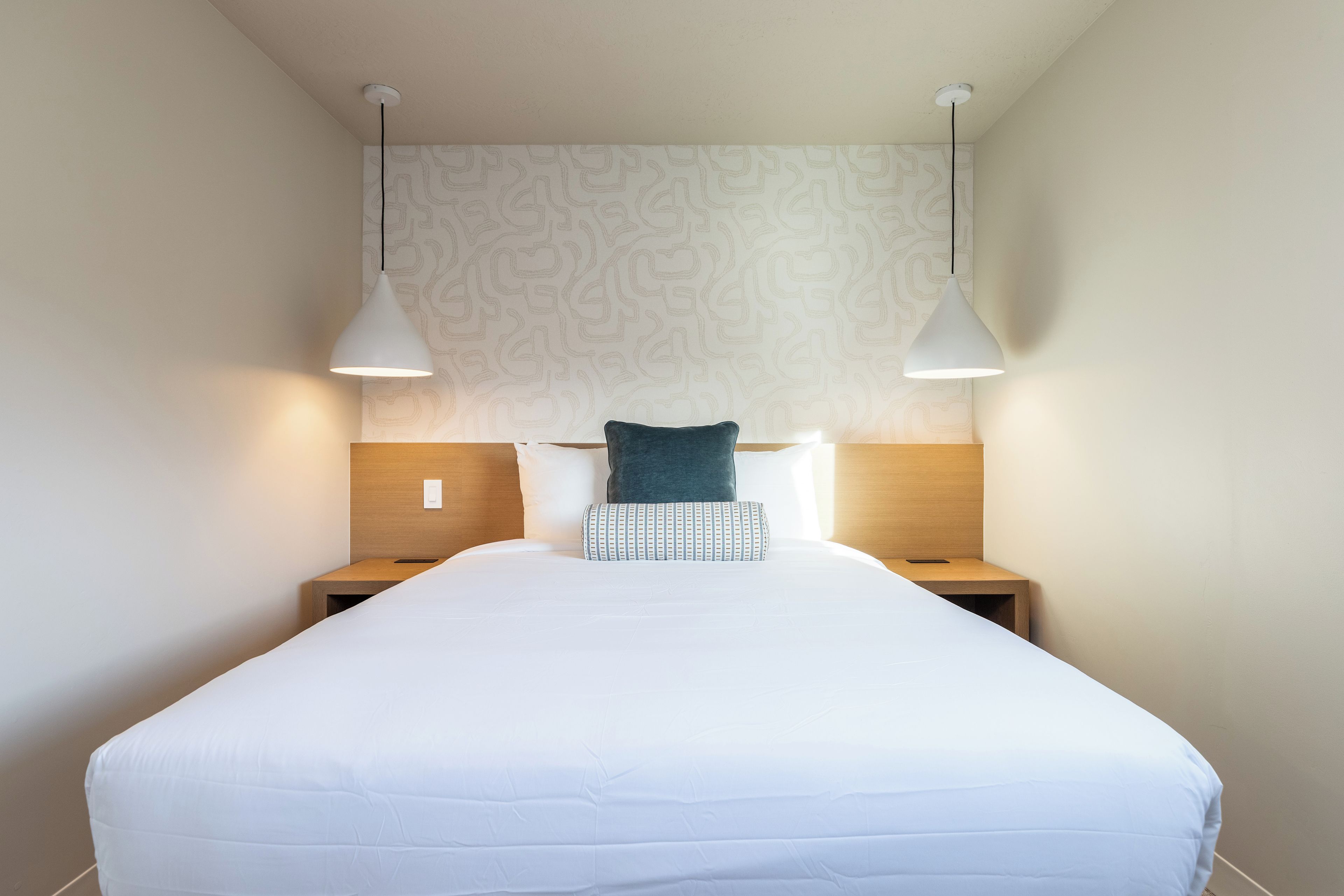 A hotel room with a large bed, two bedside tables, a patterned headboard, and pendant lights.