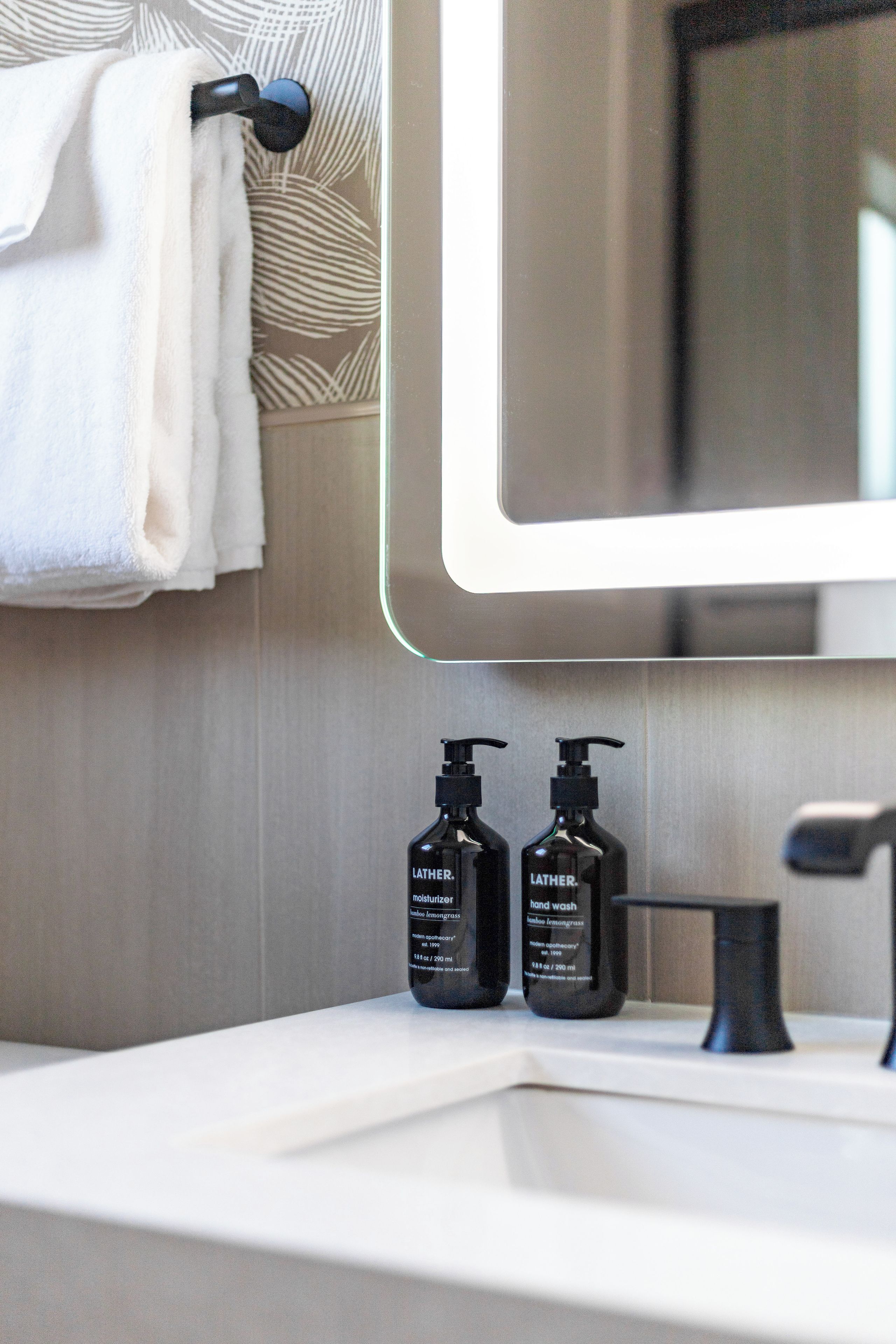A bathroom with a white sink, two black Lather hand wash bottles, and a towel hanging on a towel rack.