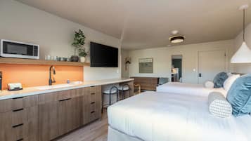 Une chambre d’hôtel moderne équipée d’une kitchenette, d’un téléviseur à écran plat, d’un lit avec des oreillers et d’une table de chevet.