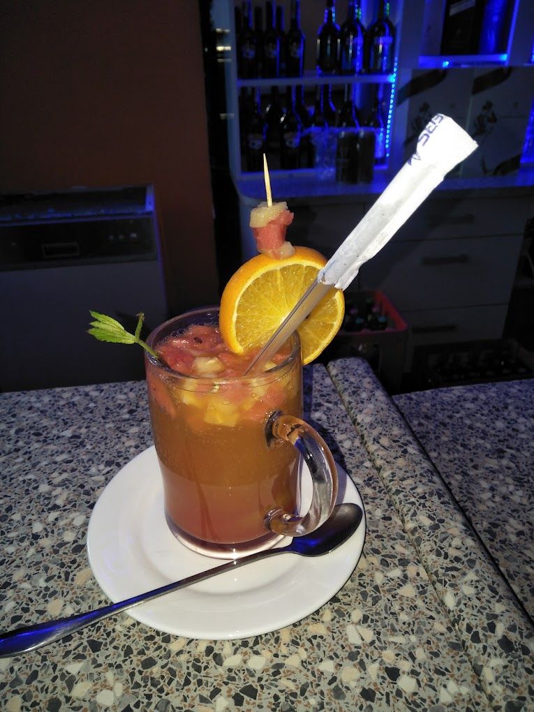 A cocktail with an orange slice and a straw on a coaster, placed on a granite table.