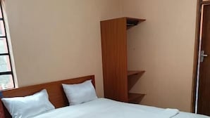 Un lit bien fait, avec une literie blanche, dans une pièce aux murs de couleur beige et dotée d’une tête de lit en bois.