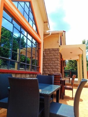 An outdoor seating area with wicker furniture and a stone wall. - Peak Meadows Hotel (Nyeri)