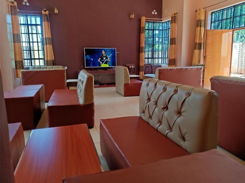 A room with a television, multiple seating options including sofas and tables, and large windows with curtains.