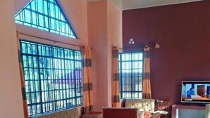 Un vaste espace salon doté de nombreux sièges, de grandes fenêtres avec des barreaux et d’un téléviseur posé sur un meuble.