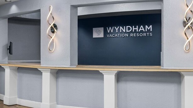 Ein Empfangsbereich der Wyndham Vacation Resorts mit dunkelblauer Wand, einer Rezeption und einer modernen Leuchte.