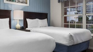 Ein Hotelzimmer mit zwei Betten, einem Nachttisch mit Lampe und einem Fenster mit Jalousien.