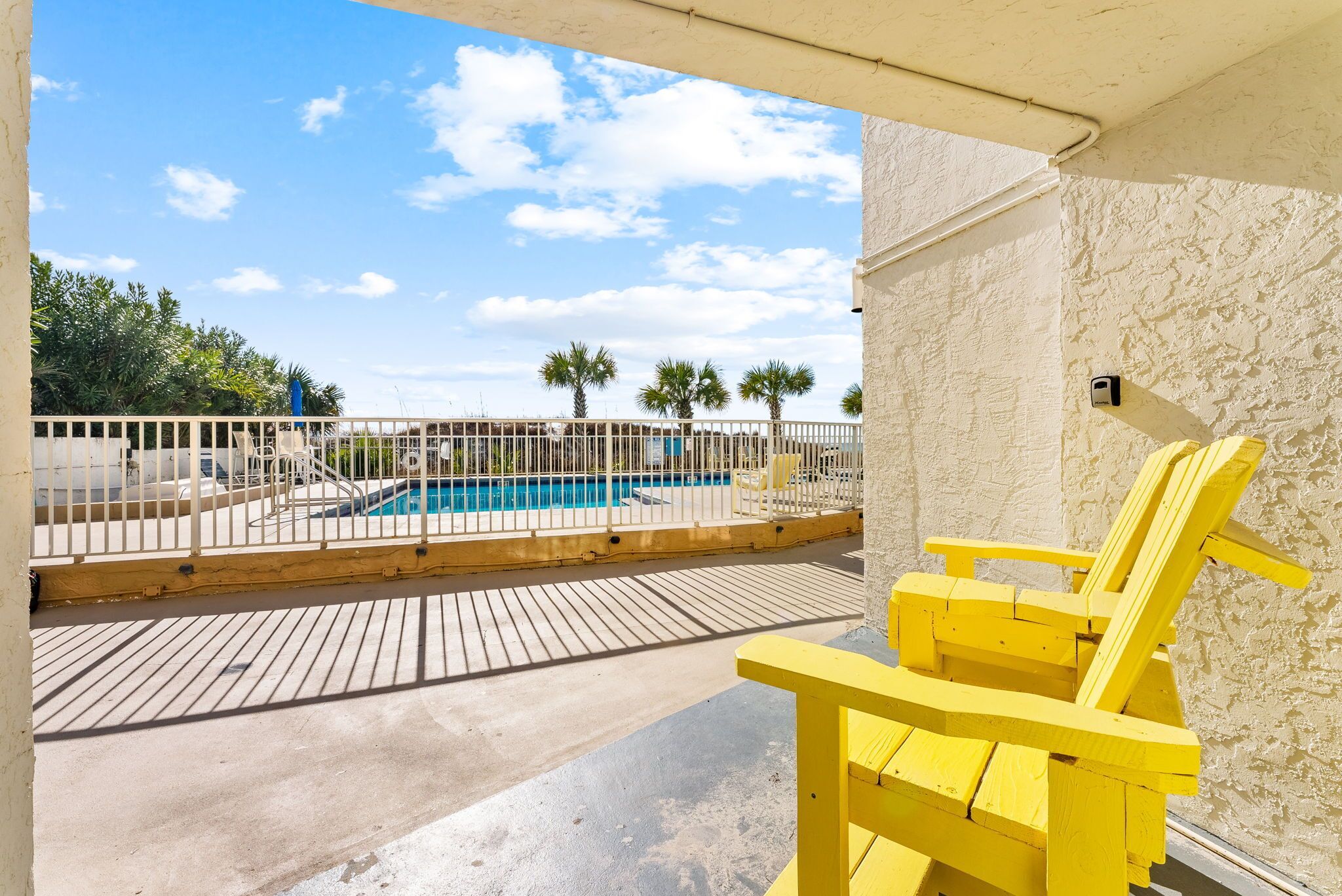 A pool area with a wooden deck, a yellow chair, and a fenced pool.