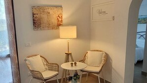 Een kamer met twee rieten stoelen, een kleine ronde tafel, een vloerlamp en een wandairconditioner.