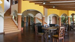 A spacious indoor area with a staircase, wooden ceiling beams, and multiple seating arrangements.