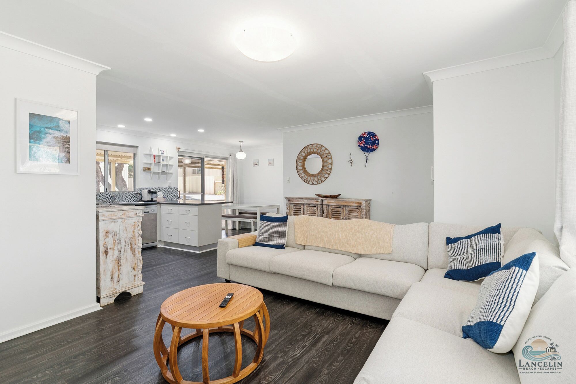 A modern living room with a sofa, a round wooden table, and a kitchen in the background.