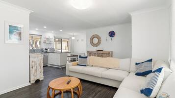 A modern living room with a sofa, a round wooden table, and a kitchen in the background.