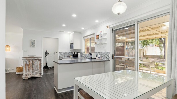 Una cocina moderna con armarios blancos, una isla central y un comedor con mesa de vidrio.