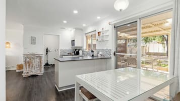 A modern kitchen with white cabinets, a central island, and a dining area with a glass table.