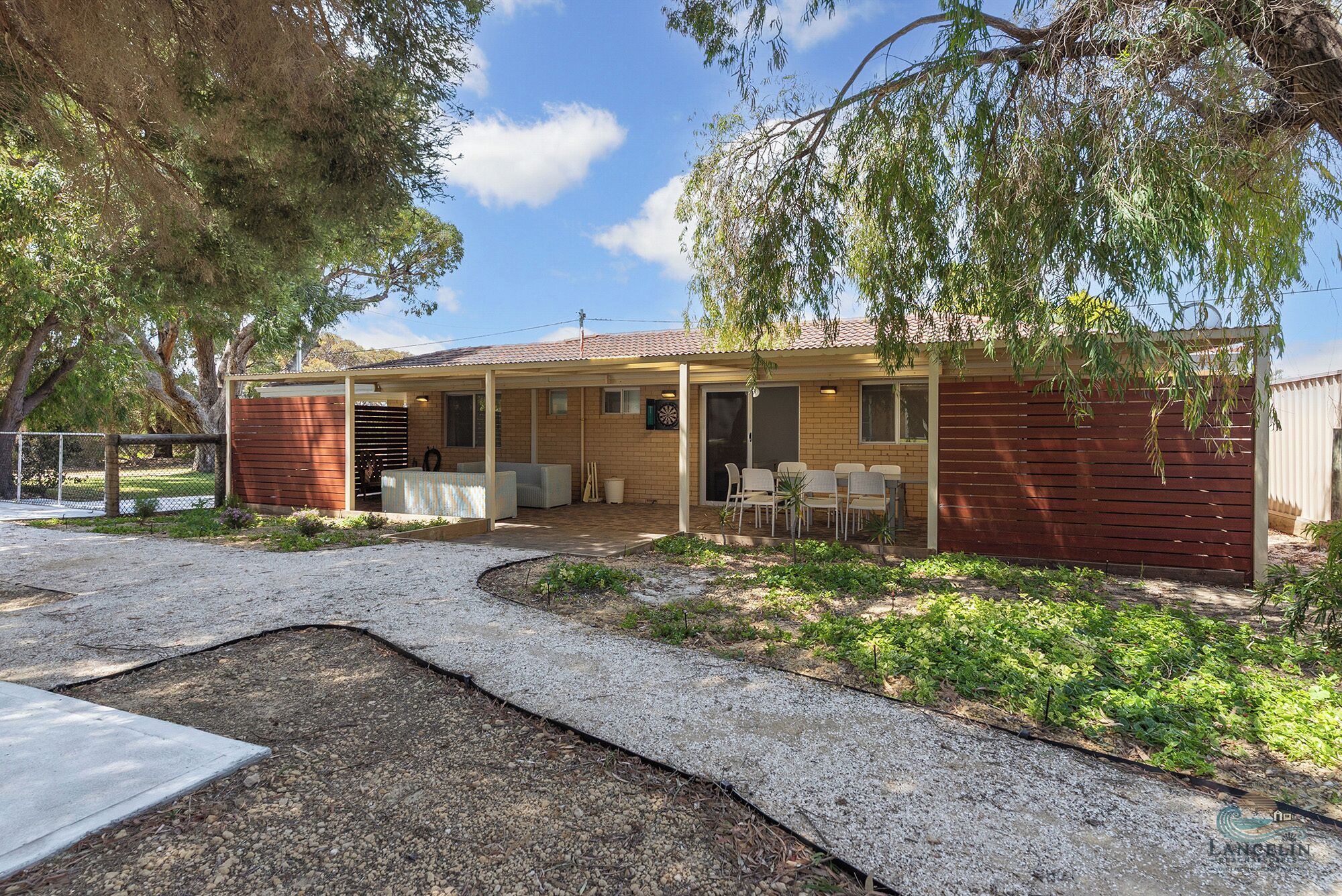 A two-story house with a covered patio, a fenced yard, and a gravel driveway.