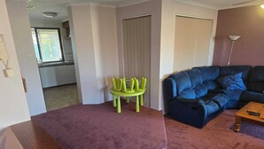 Una sala de estar con un sofá morado, un sofá azul, una mesa de centro de madera y una silla verde.